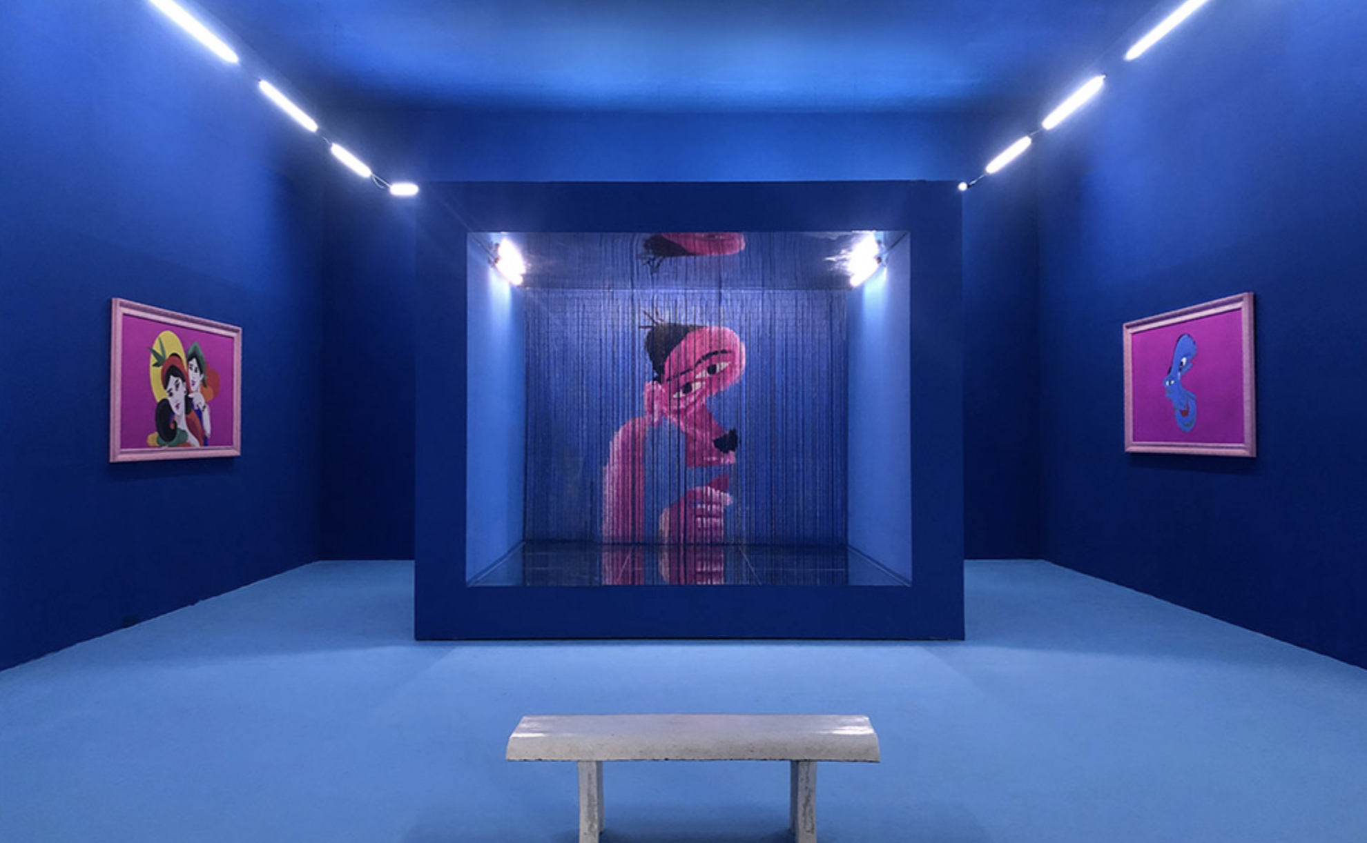 A Travipome exhibition installation with blue walls, projected artwork, and framed pieces.